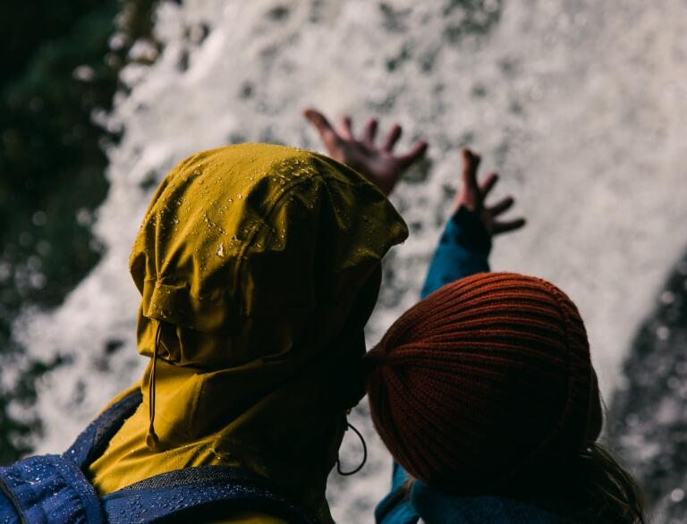 Two people reaching hands into a waterfall above them.