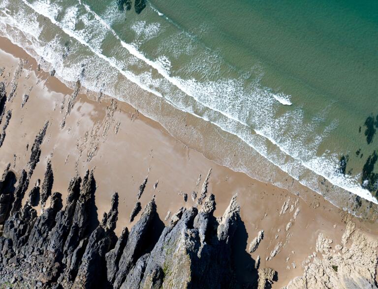 Ein Strand von oben mit Felsen, Sand und Meer.