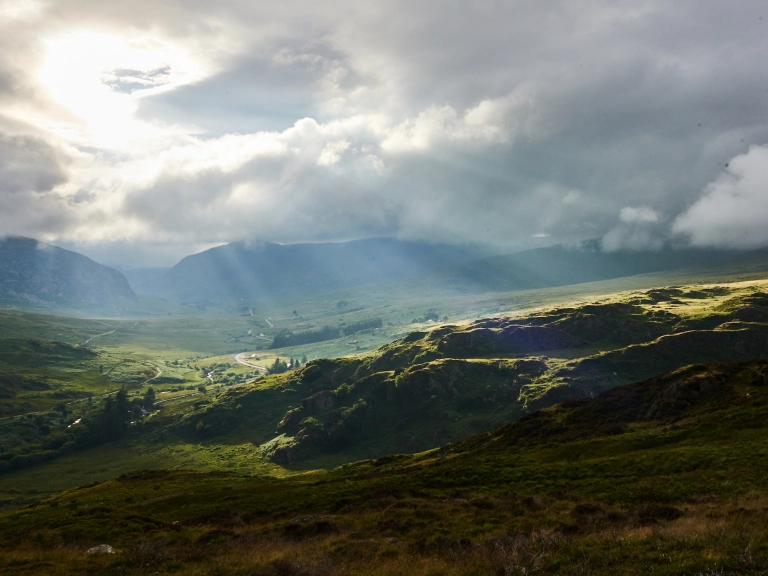 View of sun rays shining through clouds over hilly countryside