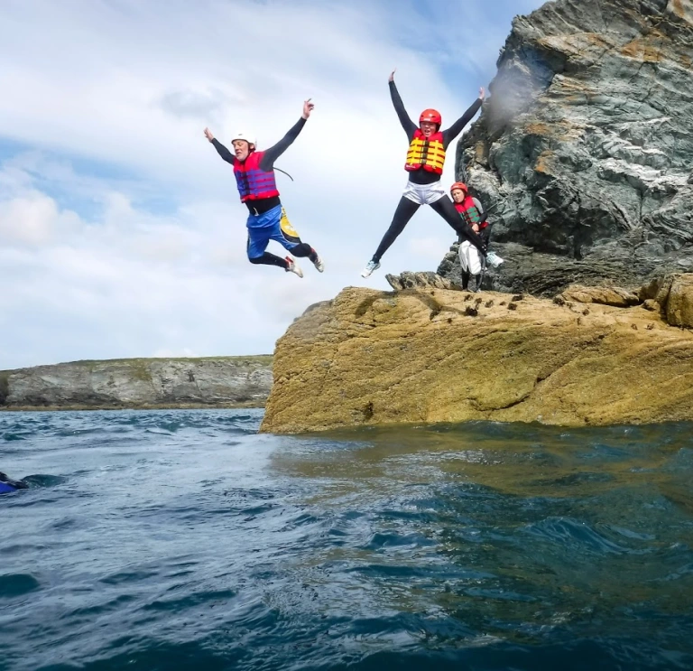 Zwei Personen mit Schwimmwesten und Helmen beim Coasteering und Sprung von einem Felsen ins Meer