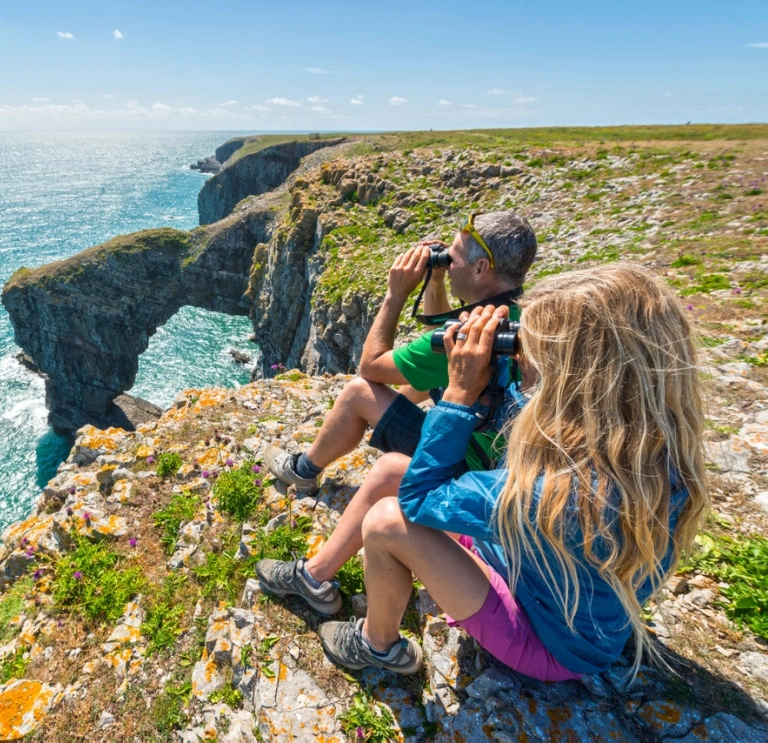 A couple on the coast path looking out to sea with binoculars.