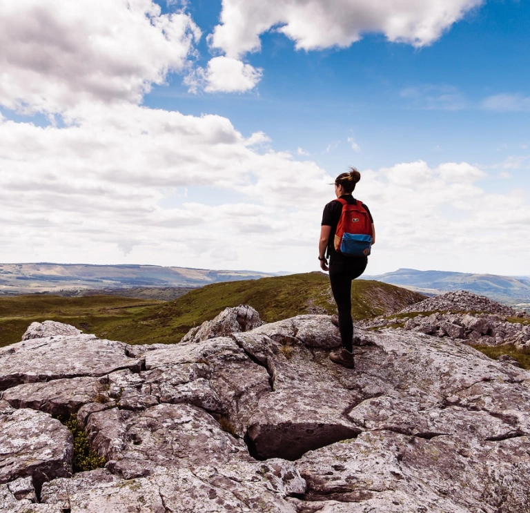 Woman hiker standing on hill, against a blue sky, looking out across the green, mountainous landscape of the Brecon Beacons, Mid Wales.