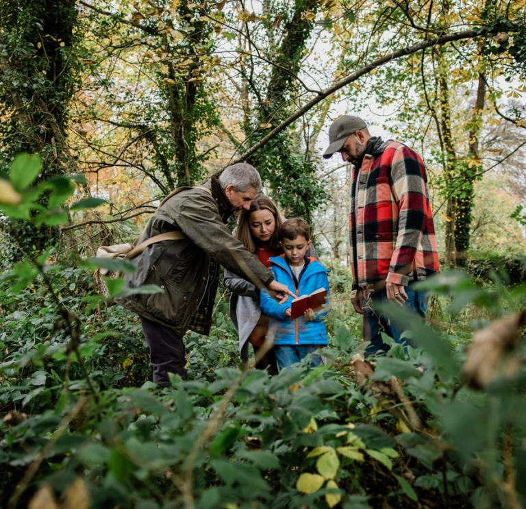 A family with a young boy In the woodswith a forager guide showing them a guide book