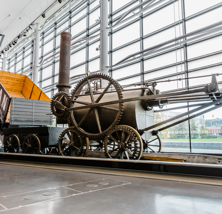 An industrial steam engine and wagon displayed in a window fronted museum.