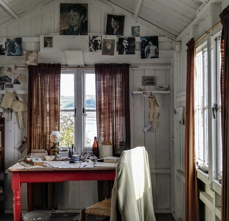 An inside scene of a shed with a writing desk and photographs on the wall.