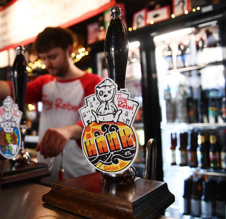 A barman pulling a pint - colourful beer taps on the wooden bar.