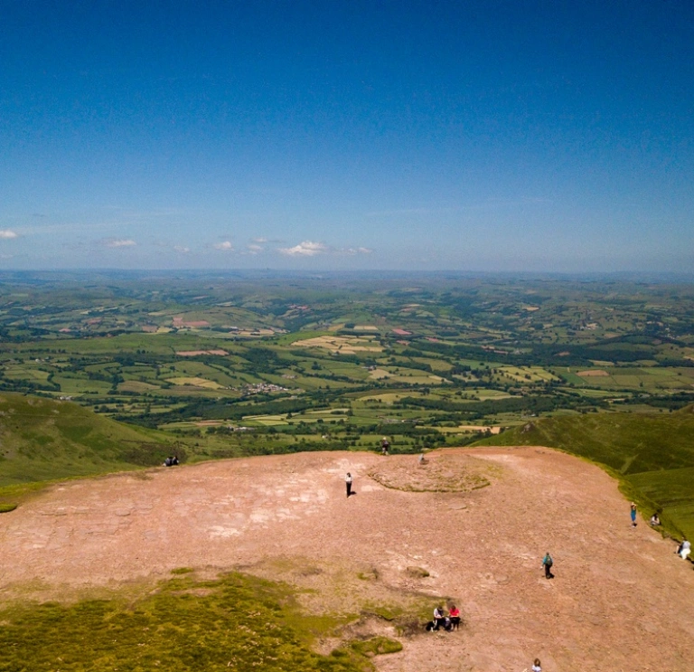 Aerial view of the green plains below from the top of Pen y Fan with blue skies.