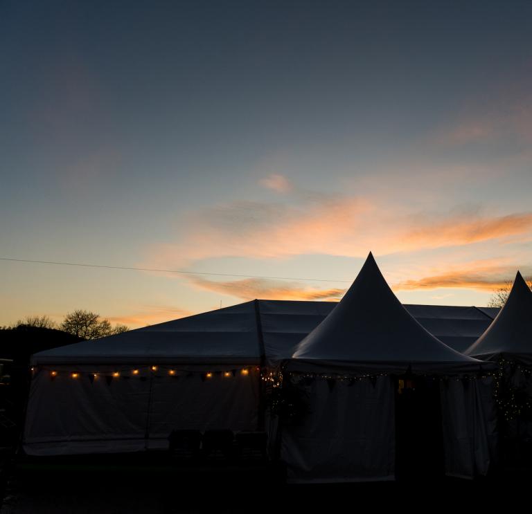 A tent with fair lights and a sunset in the background.