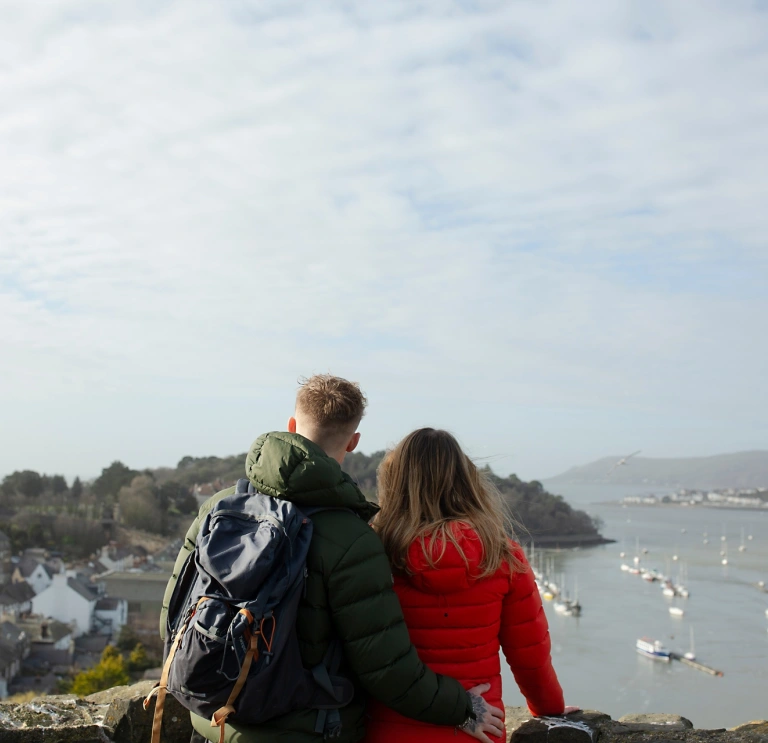 man and woman stood in castle with view of sea and boats.