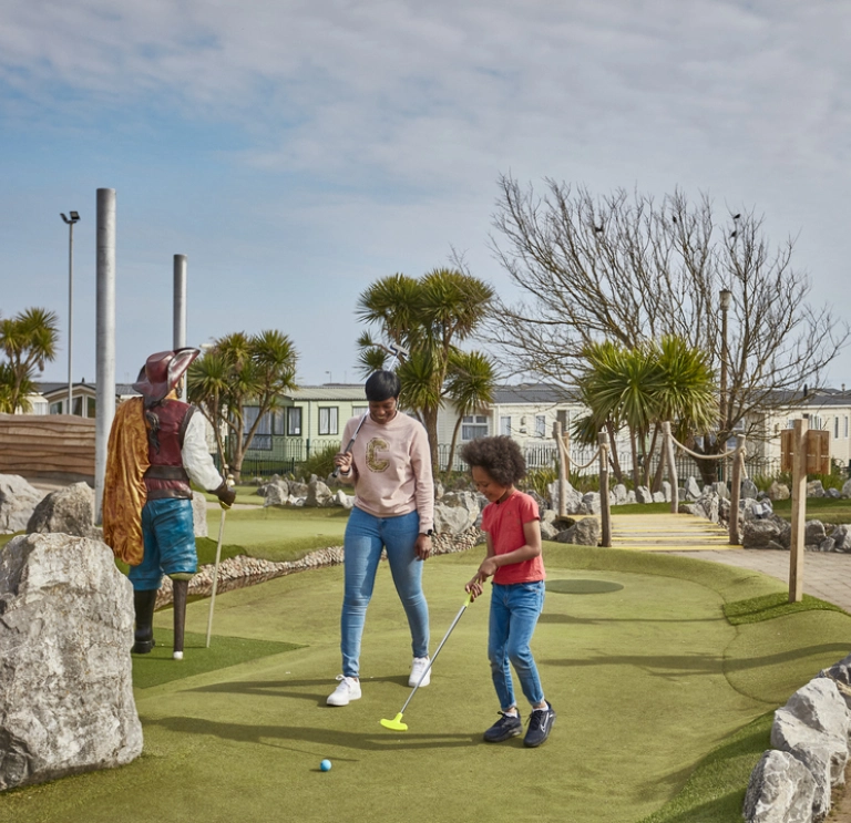 Mum and son play crazy golf on a sunny day whilst dad and daughter watch 