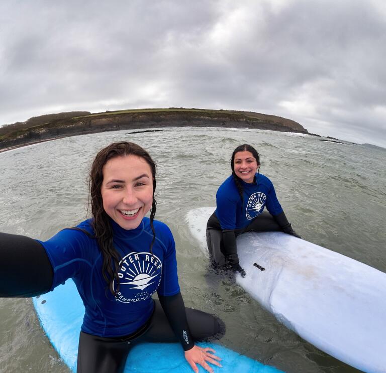 two women sat on surf boards in the sea.