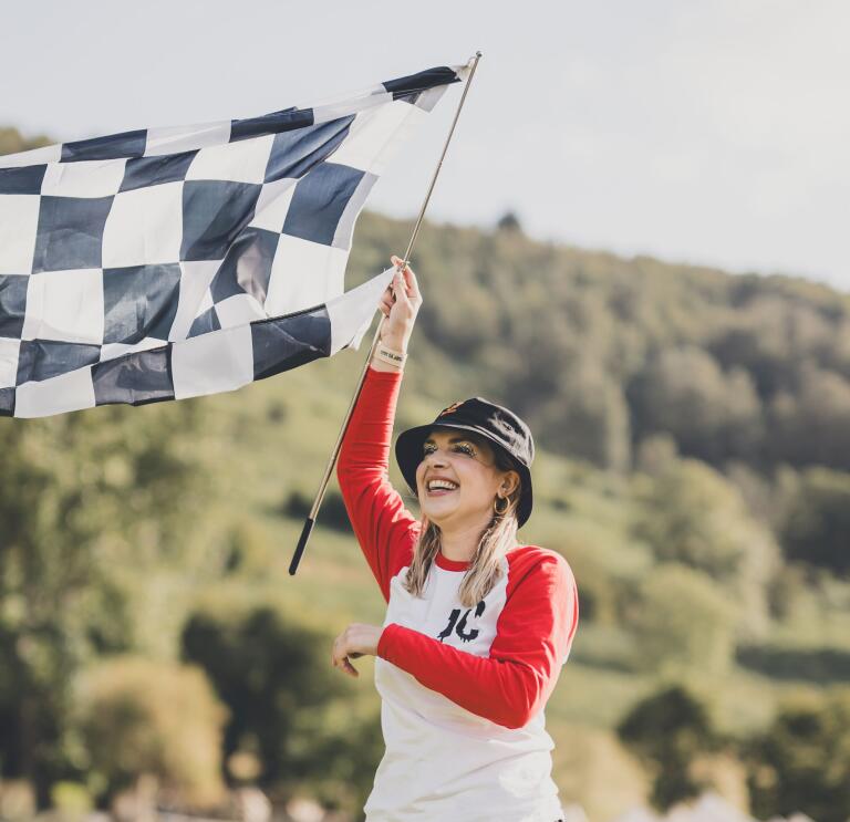 A smiling person waving a chequered racing flag at a festival