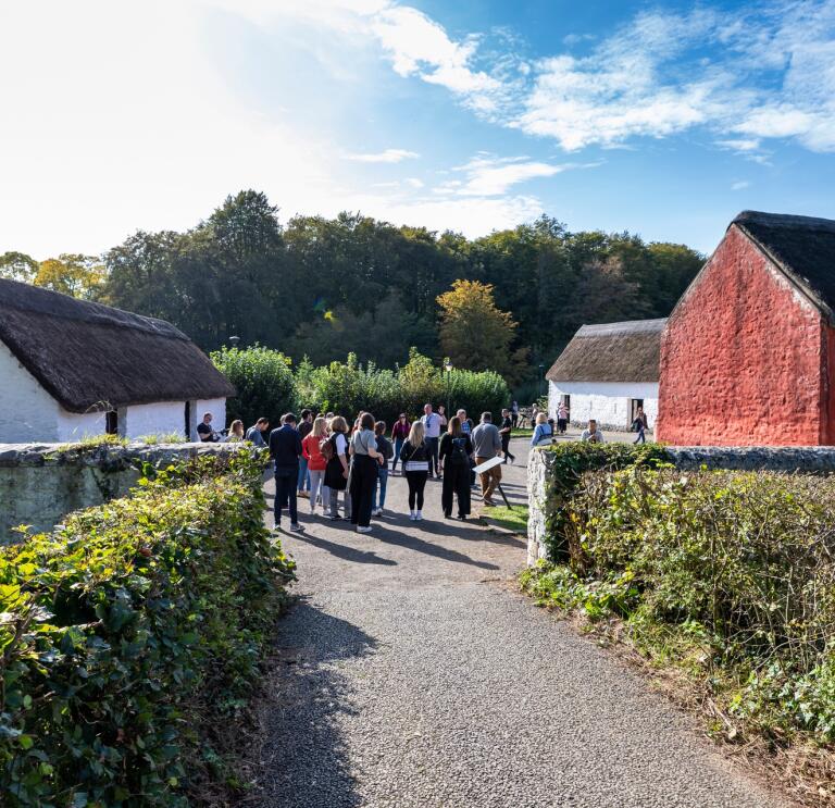 A group of people looking round an open air museum with reconstructed farmhouses.