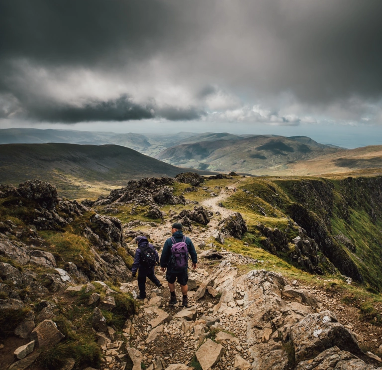 Two people walking along a mountain ridge.