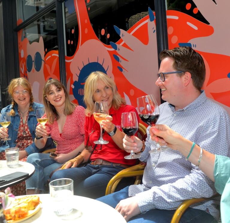 people sat at tables holding glasses on wine and smiling.