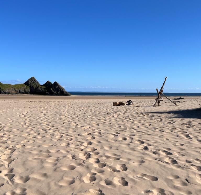 A wide, sandy beach with jagged cliffs one side and sand dunes the other.