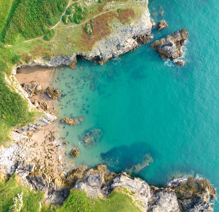 aerial view of sandy beach, green pathways and clear blue sea.