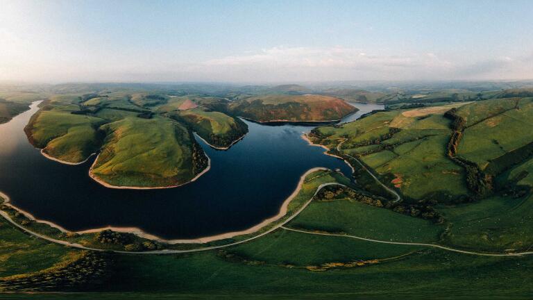 Overhead panorama of a glassy reservoir and sundrenched green hills