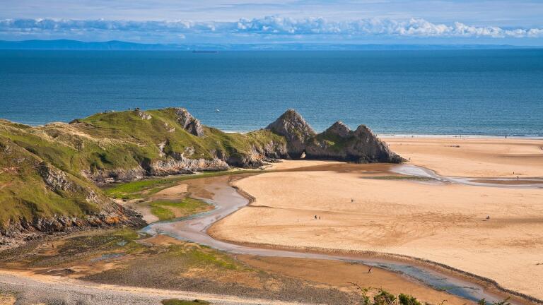 Tide out at Three Cliffs Bay with rivulets of sea water left on the sandy beach.