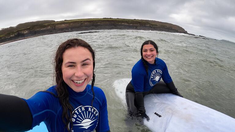 two women sat on surf boards in the sea.