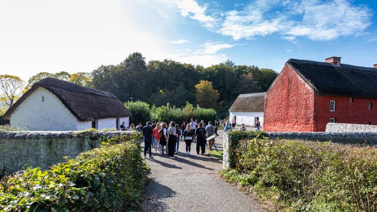 A group of people looking round an open air museum with reconstructed farmhouses.
