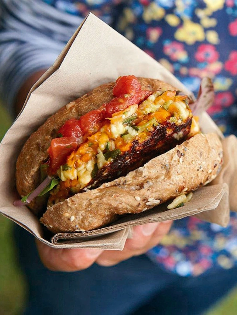 Burgers held in a napkin, filled with bacon, cheese and garnish.