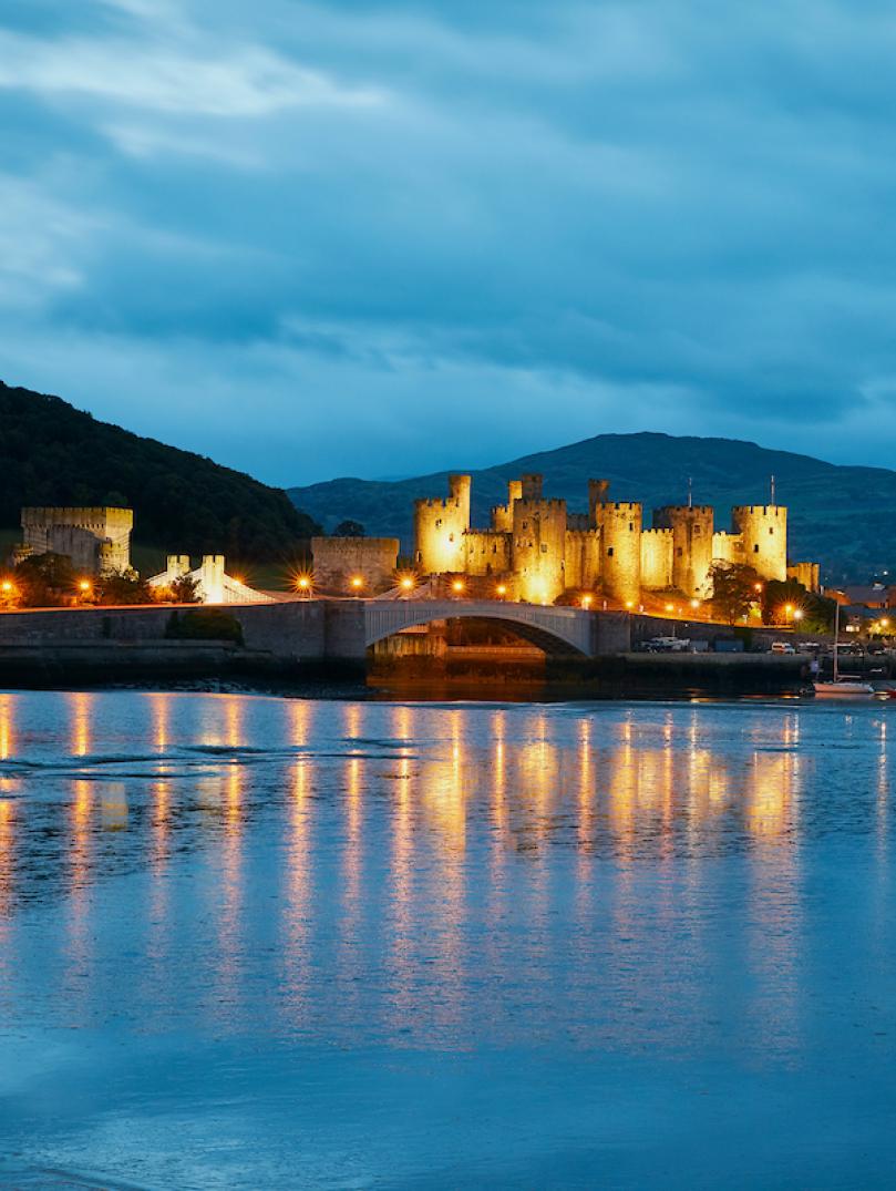 Castell Caernarfon (Caernarfon Castle) lit up at night and reflection in water.
