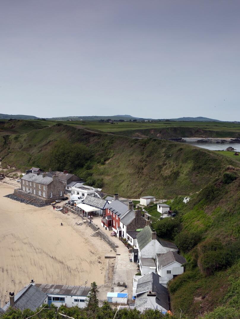 buildings on the beach, backing onto green hills.