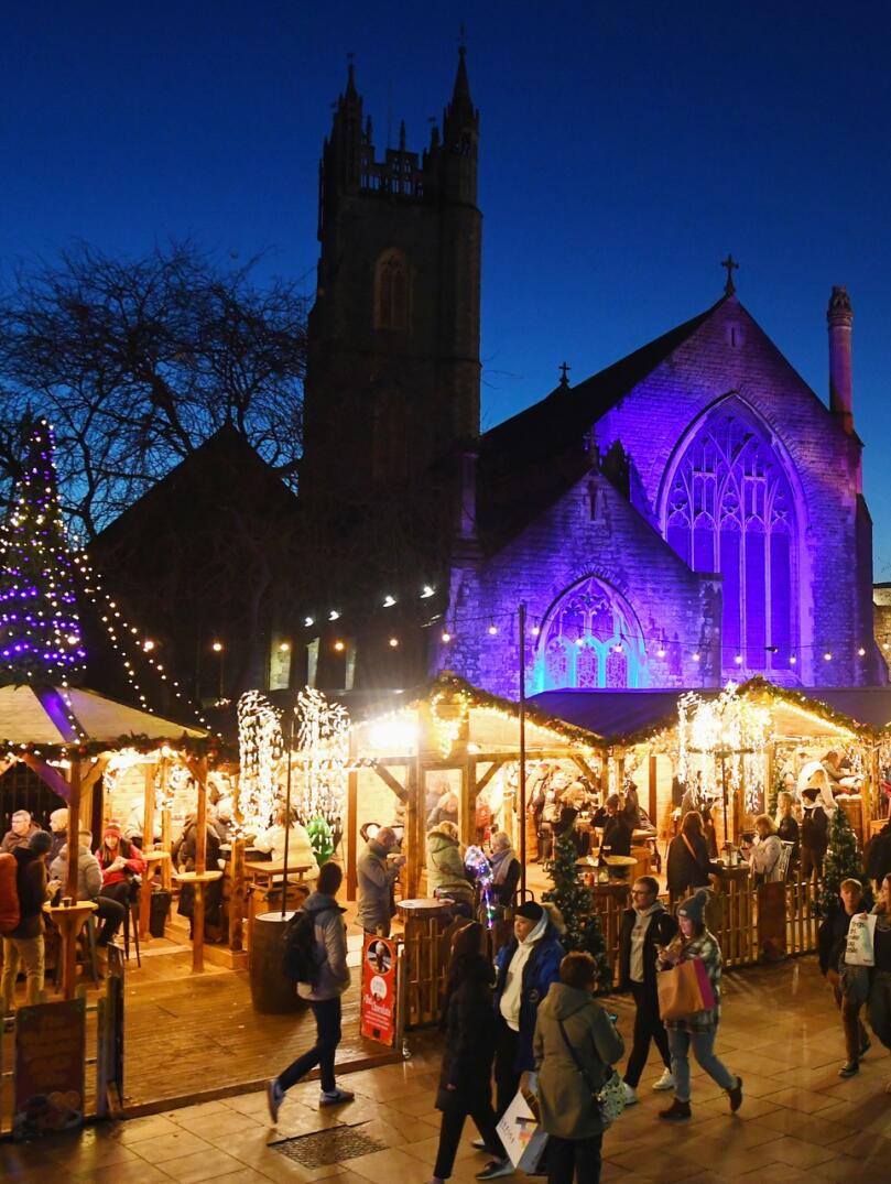 A row of Christmas market stalls in a busy street at night.