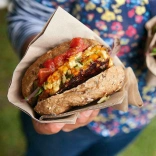 Burgers held in a napkin, filled with bacon, cheese and garnish.