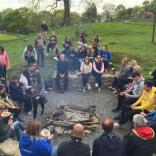 A group of people sitting around a campfire eating a barbecue.