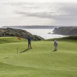 Two people playing golf on the green with views of the sea and mountains in the background.