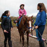 A young lady being assisted to ride a horse.