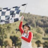 A smiling person waving a chequered racing flag at a festival