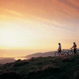 Two mountain bikers watching a sunset over the Mawddach eastuary.