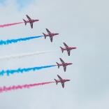 Five areoplanes, the Red Arrows, flying in an arrow formation with red white and blue vapour trails. 