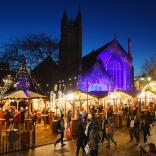 A row of Christmas market stalls in a busy street at night.