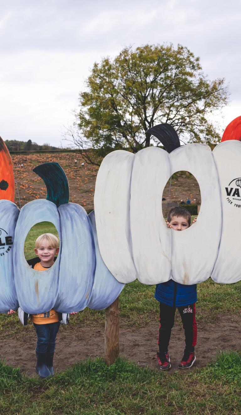 children inside pumpkin cut outs posing for photo.